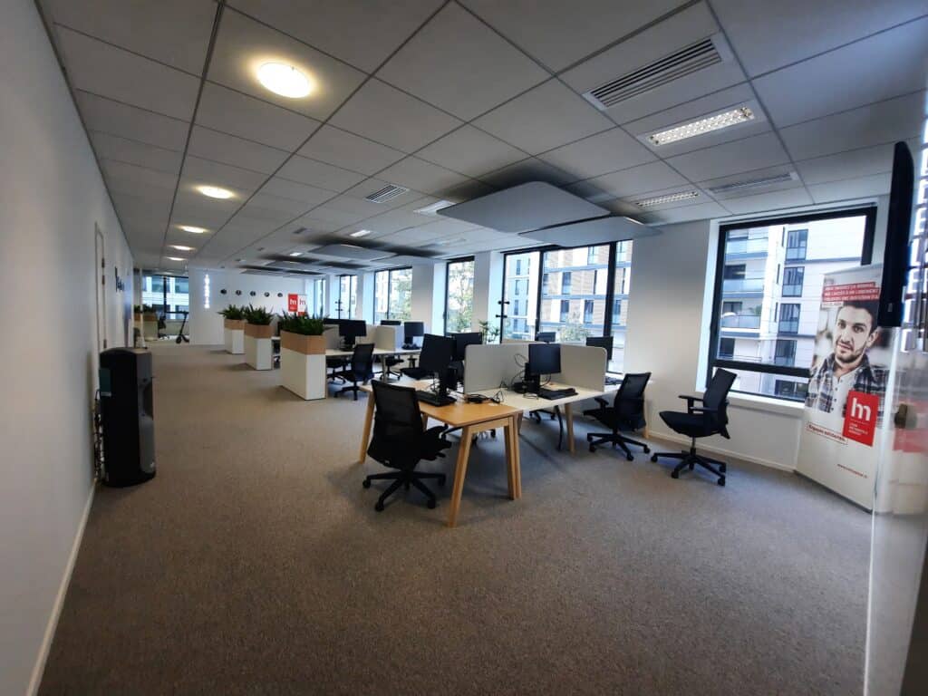 Bureau Open Space Moderne et Postes de Travail Lumineux Bureau open space moderne avec postes de travail ergonomiques, plantes vertes et vue urbaine, affiche LM Habitat.